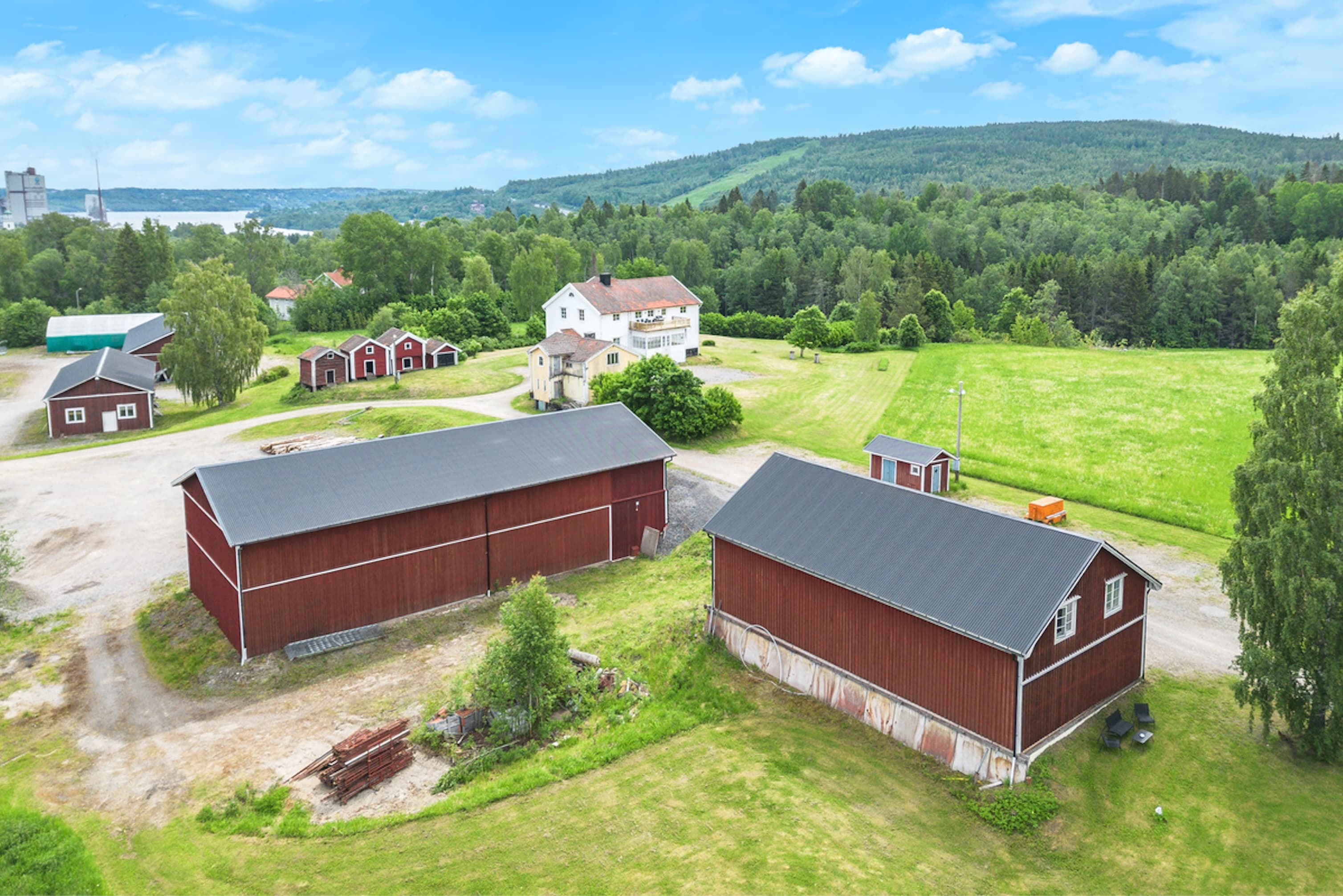 Åkermark mot öst, syd samt nord väst. Baksida Garagebyggnad, baksida Maskinhall, gavel Såghus med ingång till Snickeri, gavel Förrådsbyggnad, framsida nedre Bostadshus.